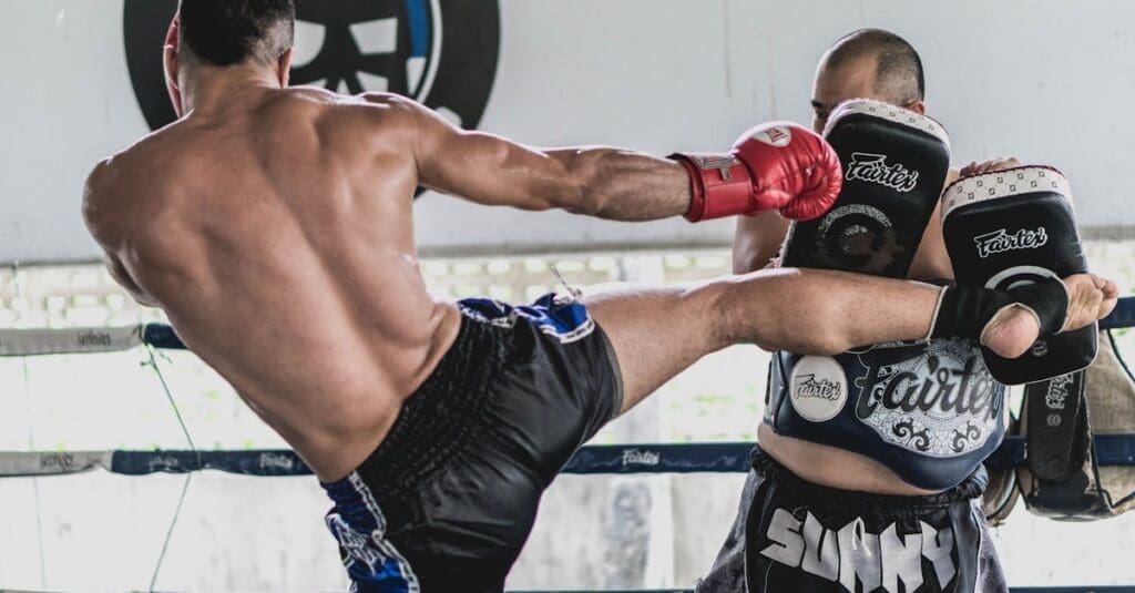 An instructor holds large kicking shields inside a boxing ring, a key lesson in a beginner kick boxing guide.