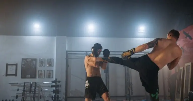 Shirtless athletes spar with high kicks inside a misty training facility, showcasing advanced drills for a beginner kick boxing guide.