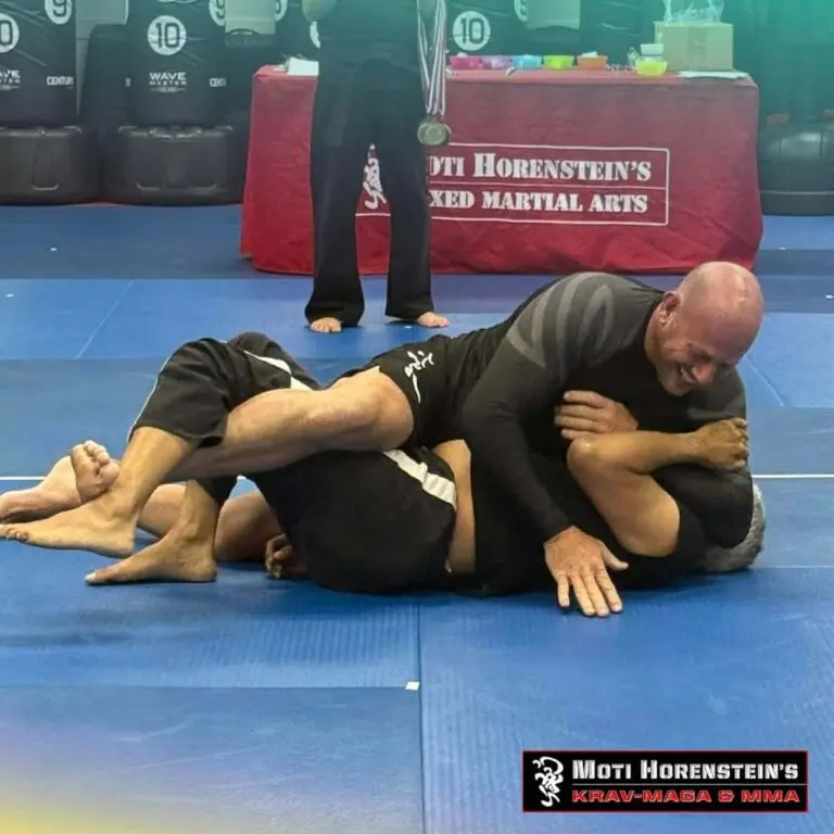 Two martial arts practitioners demonstrating ground control and leg positioning during a grappling drill focused on jiu jitsu guard retention basics.