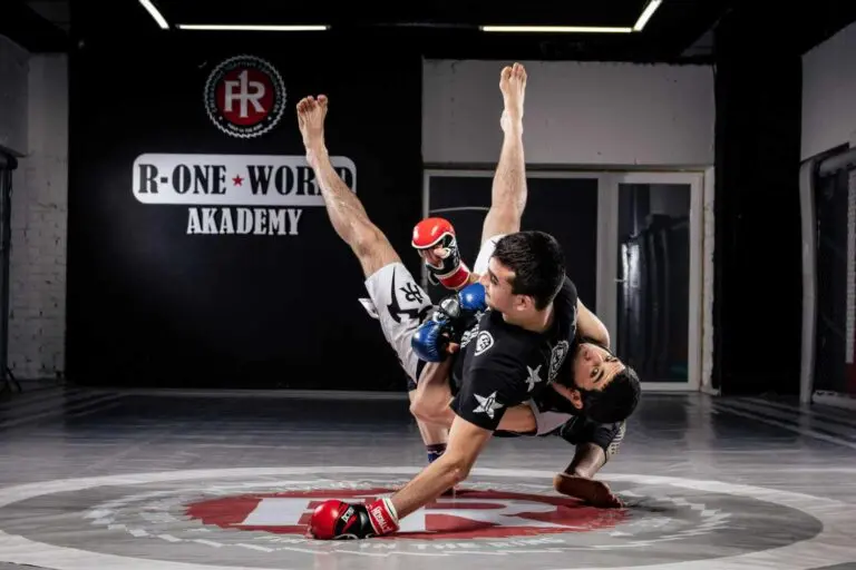 Two martial artists executing a sweep and ground roll on the academy mat MMA beginner fundamentals