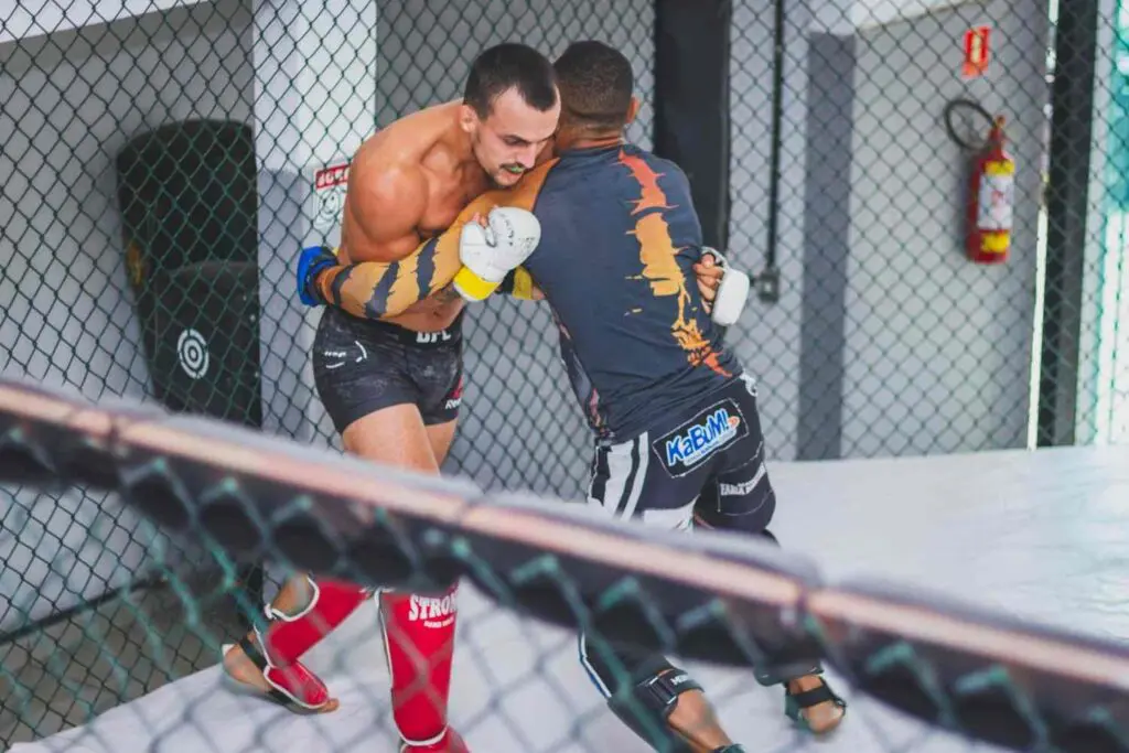 Two martial artists practicing clinch work against the cage wall MMA beginner fundamentals