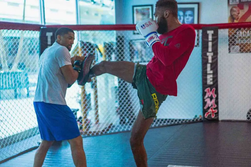 Fighter throwing a roundhouse body kick into focus mitts held by a coach MMA beginner fundamentals