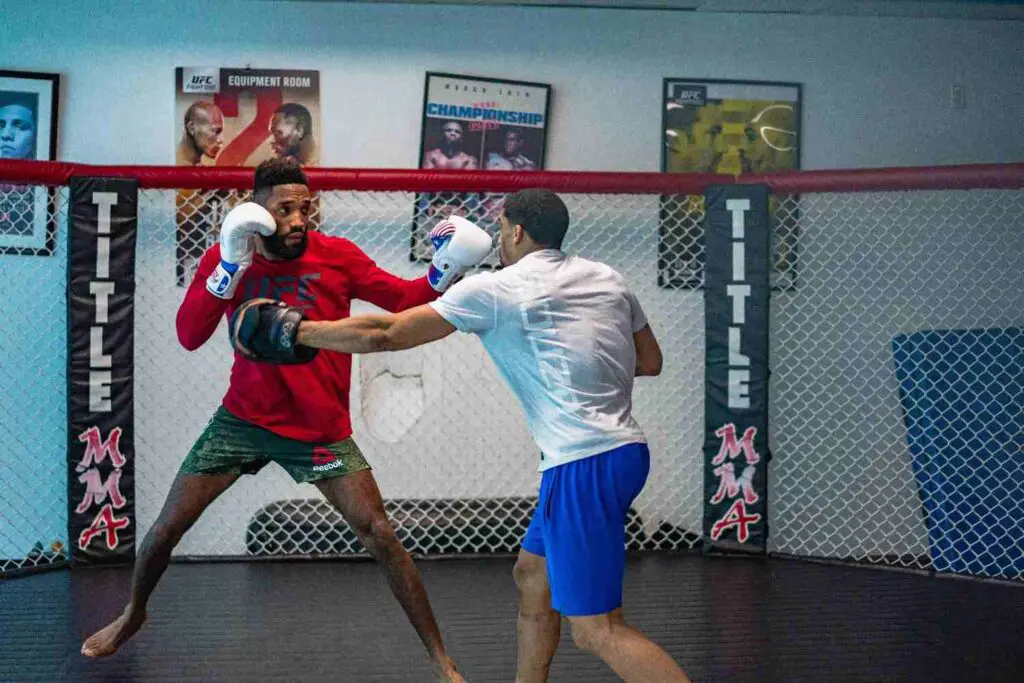 Fighter throwing a straight lead punch into training focus mitts in an MMA cage MMA beginner fundamentals