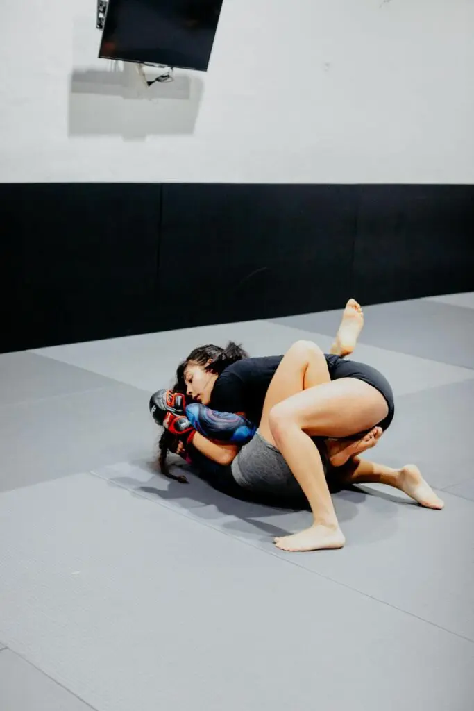 Two fighters executing a body-lock takedown drill inside the cage MMA beginner fundamentals